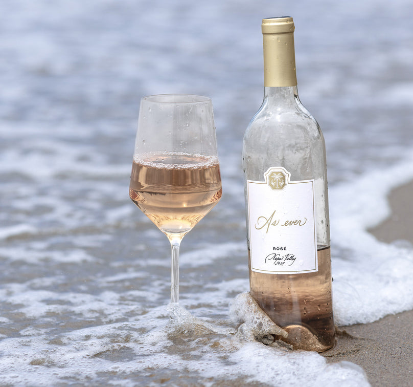 Bottle and glass of As ever Rosé wine on a beach with ocean waves in the background