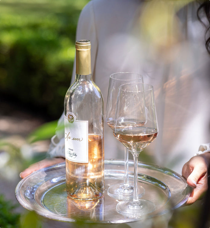 Bottle and two glasses of As ever Rosé wine on a tray with a blurred outdoor background