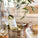 Bottle of As ever Sauvignon Blanc in a metal ice bucket with a glass on a table, surrounded by greenery