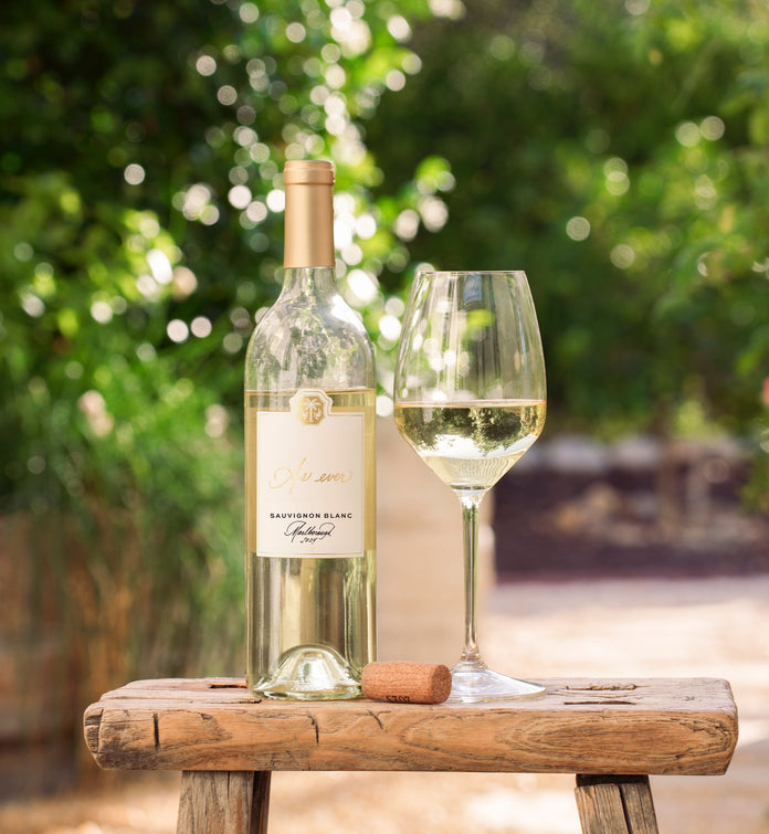Bottle of As ever Sauvignon Blanc on a wooden stool with a blurred green background
