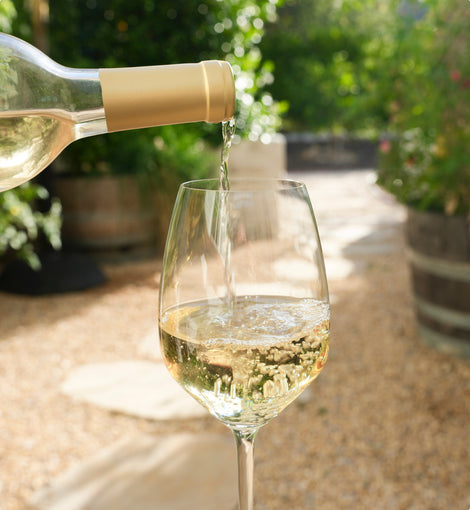 Bottle of As ever Sauvignon Blanc being poured from a bottle into a glass with a garden background