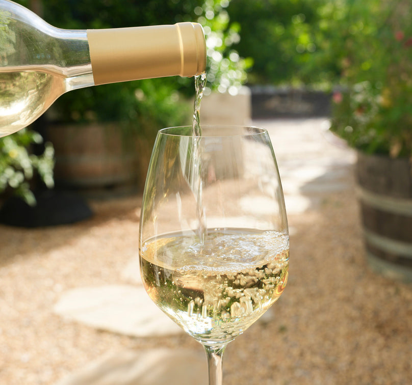 Bottle of As ever Sauvignon Blanc being poured from a bottle into a glass with a garden background