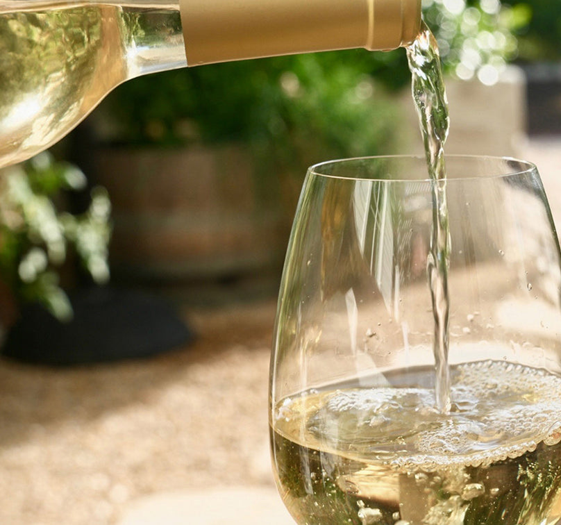 Bottle of As ever Sauvignon Blanc being poured from a bottle into a glass with a garden background